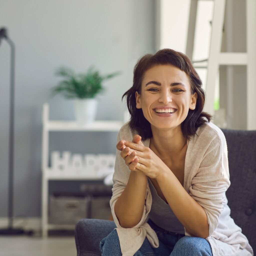 Happy woman sitting in an armchair with clasped hands smiling.
