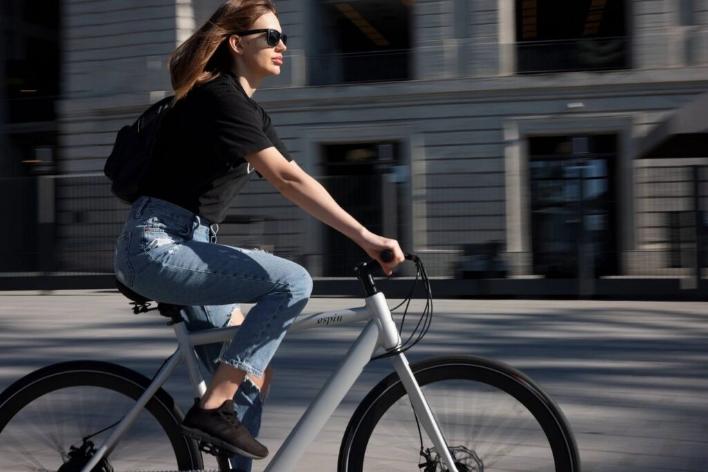 A woman in black shirt and in jean, biking on the road.