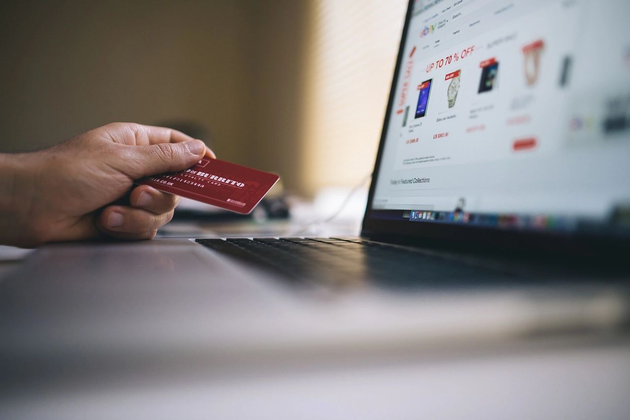 A photo of a laptop that has Online Shopping website pulled up with a hand holding a credit card on the left. 