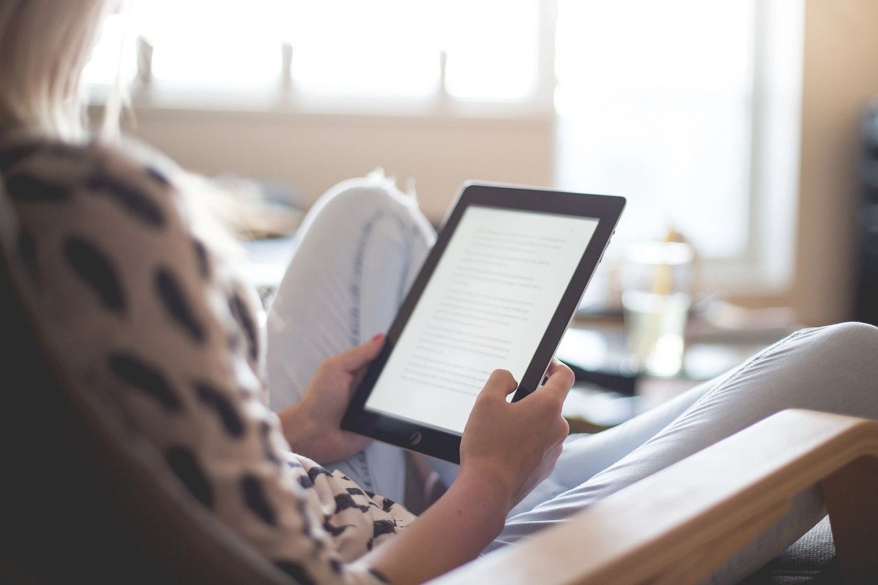 A woman sitting on her sofa, holding a kindle, reading.